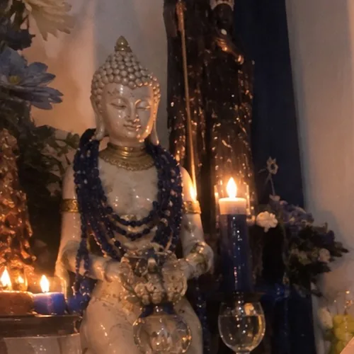 Altar da Day com uma estátua branca de colares azuis, velas acesas e uma taça de água