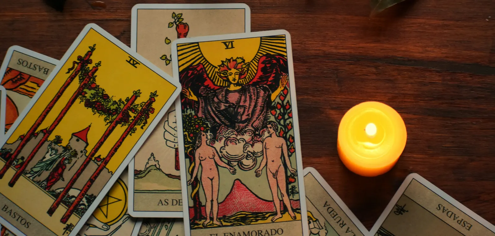 Cartas de tarô espalhadas sobre a mesa de madeira, ao lado de uma vela acesa